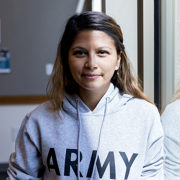 A woman wearing an Army sweatshirt standing in front of a bulletin board