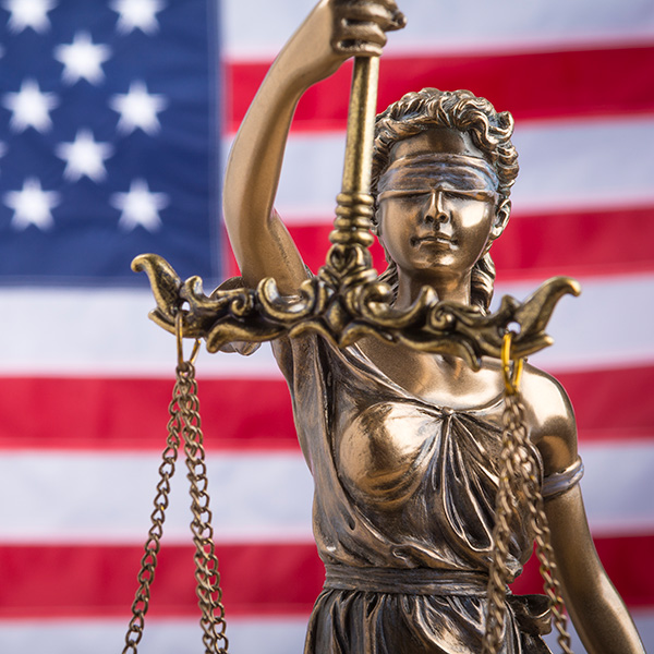 Bronze Lady Justice statue standing in front of an American flag
