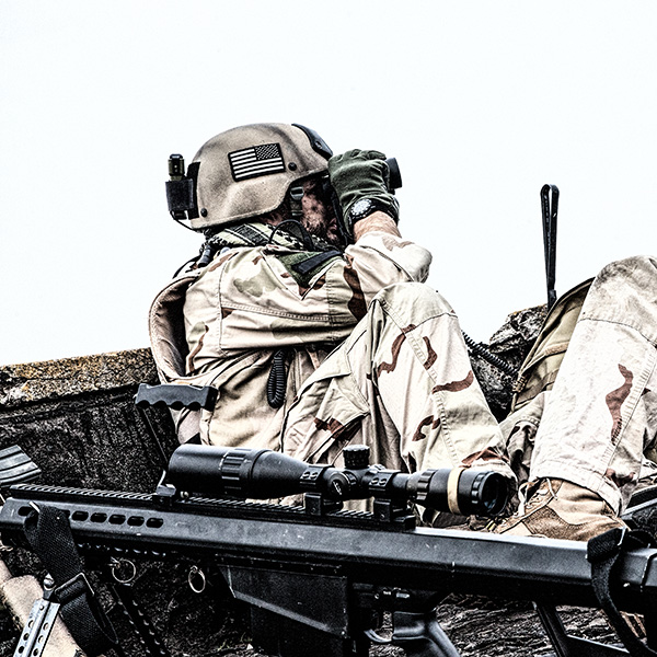 A person wearing military gear and looking through binoculars