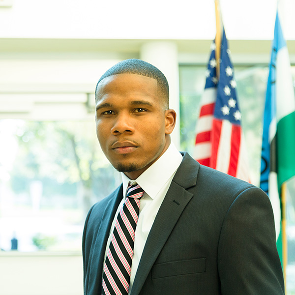 A man wearing a suit and tie, standing in front of an American flag